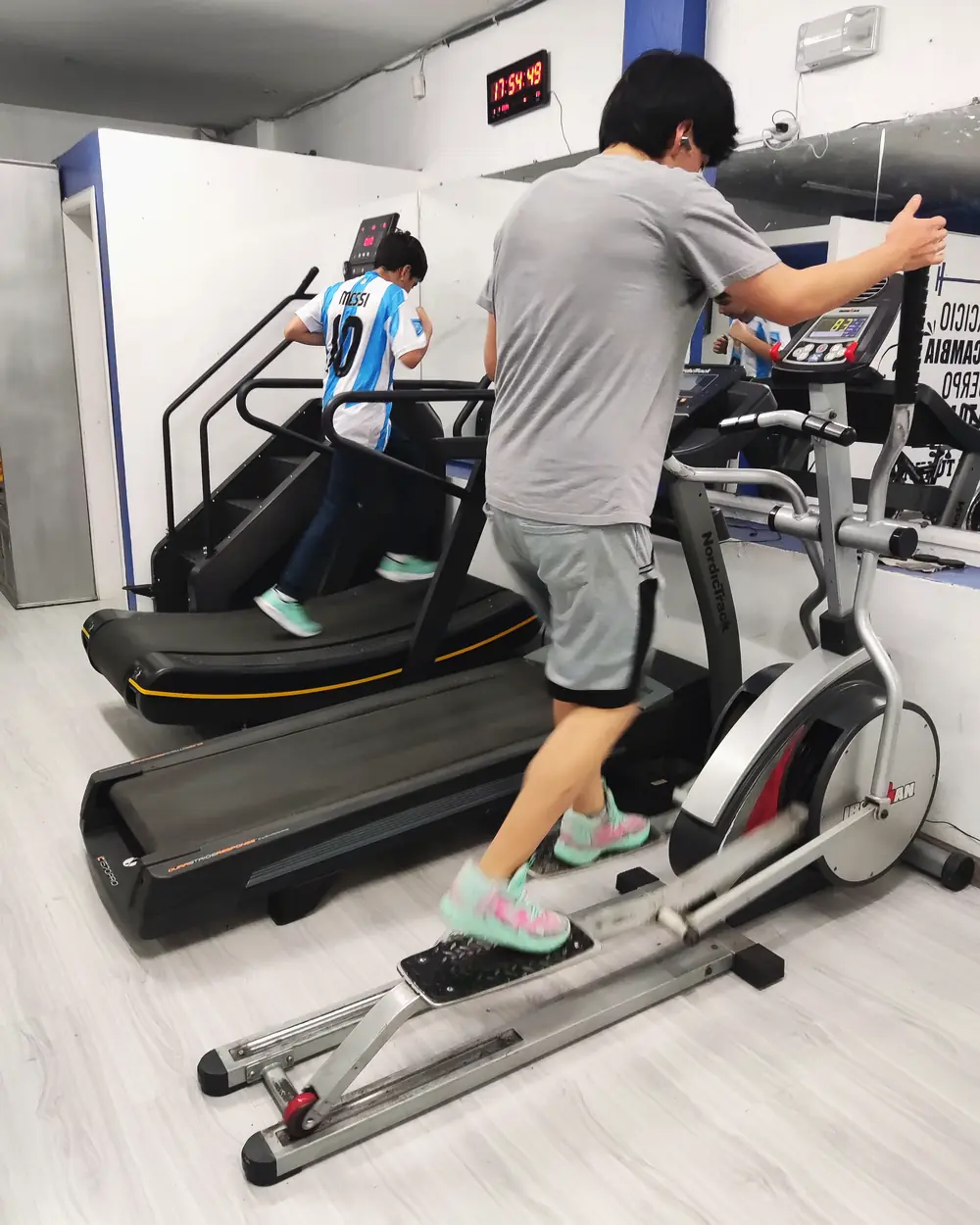 Un niño corre en la cinta curva y un joven usa la elíptica, en la zona de cardio.