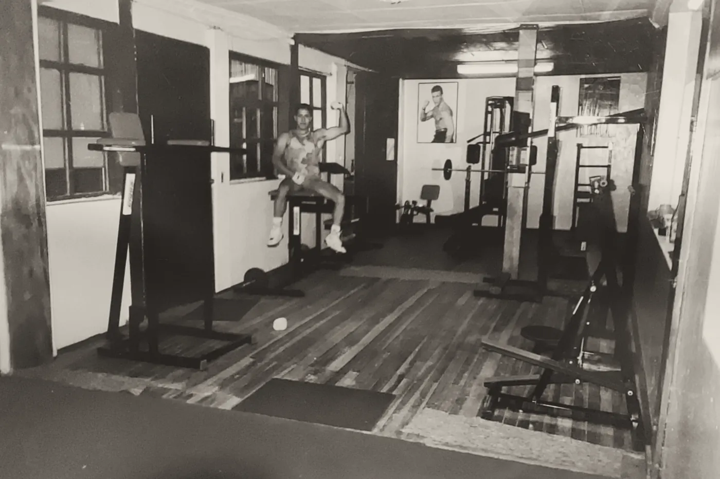 Raúl, joven, sentado en una máquina del primer gimnasio, con suelo de madera y un póster en la pared.