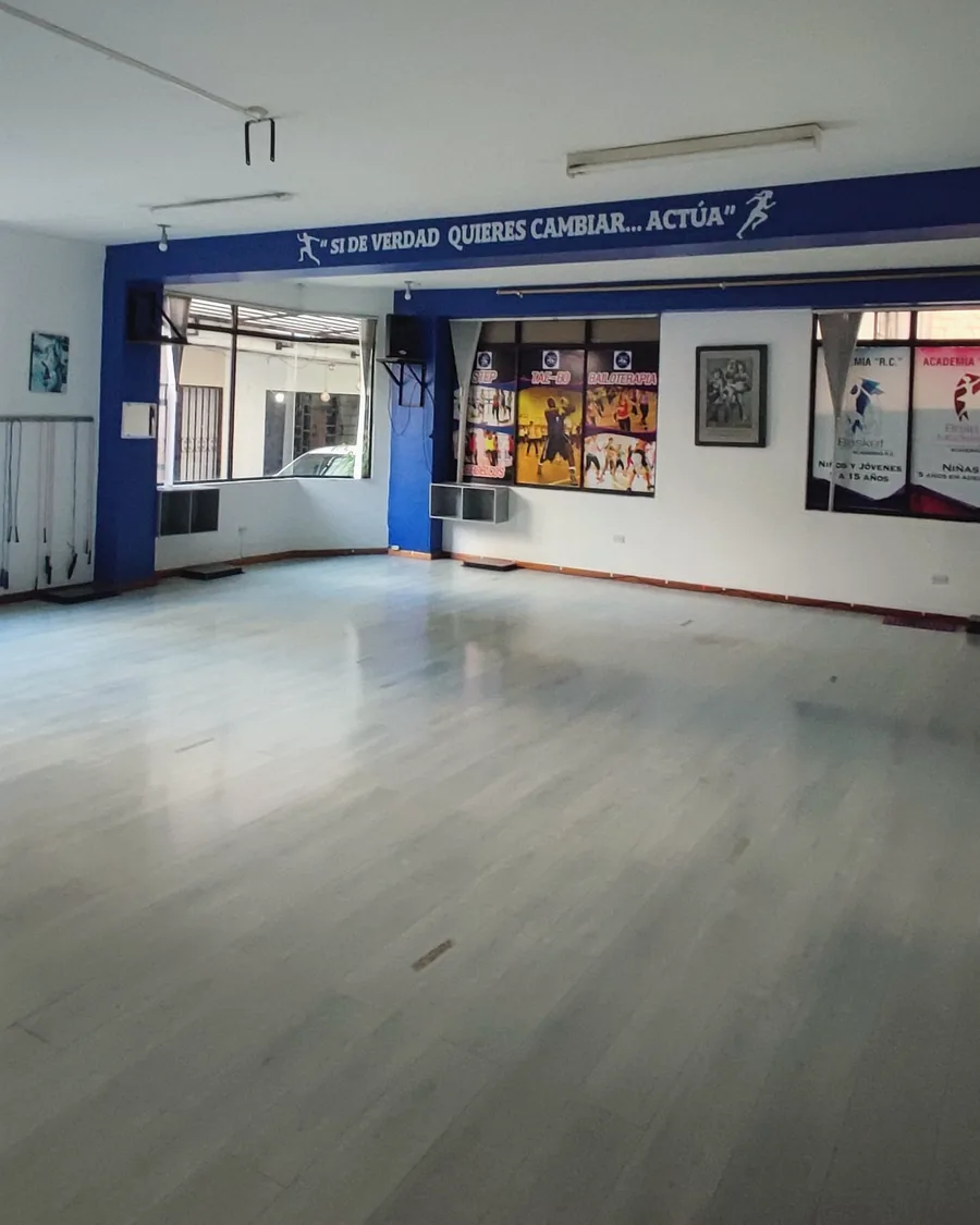 El área amplia vacía: suelo de madera clara, columnas azules y espacio de sobra para las clases.